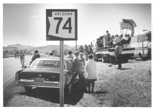 In a black and white photo from 1974, people gather at the opening of a rural highway.