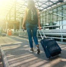 A woman walks with a carry-on bag at an airport.