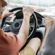 A person in the passenger seat pointing at a young driver
