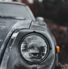 The headlight of a black car showing its age with peeling paint.