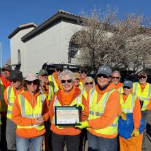 A group of people in orange and yellow safety vests pose for a photo.