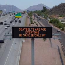 A digital message board on the highway encourages motorists to wear a seatbelt.