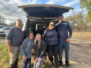 A group of people pose together in front of the trunk of a mini van.