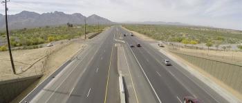 A wide highway in a desert landscape, with cars driving and mountains visible in the distance.