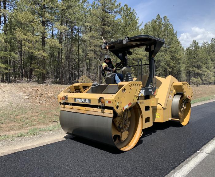 A roller flattens and smooths new asphalt on a highway.