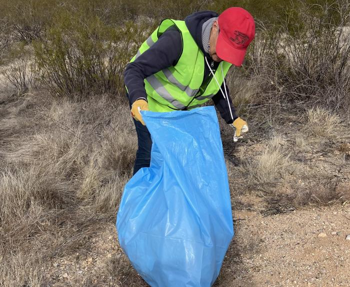 A volunteer collects litter from a highway roadside.