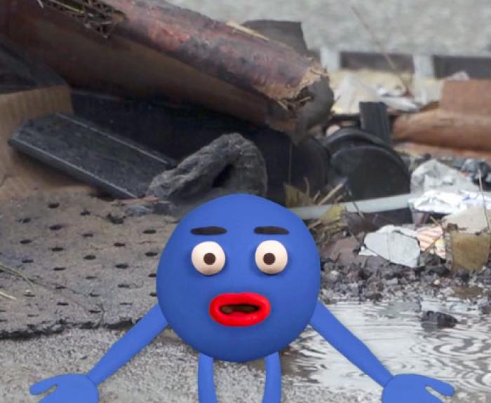 An anthropomorphic rain drop standing in front of a puddle of water, surrounded by various debris.