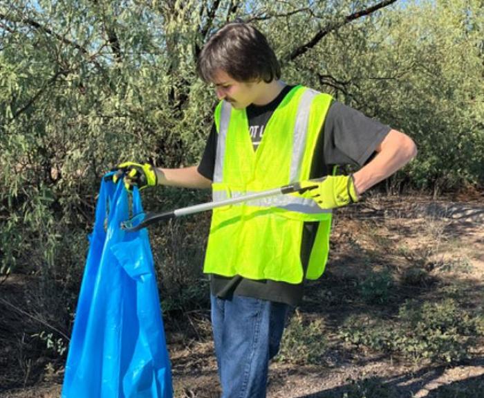 A man in a reflective yellow vest picks up litter along a highway.