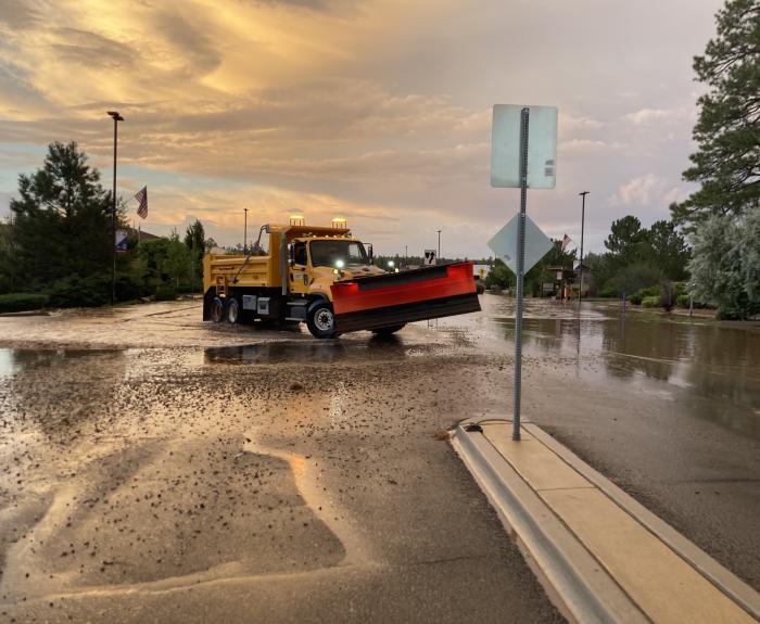 A snow plow in a flooded street clears water and debris from the roadway after rainstorm.