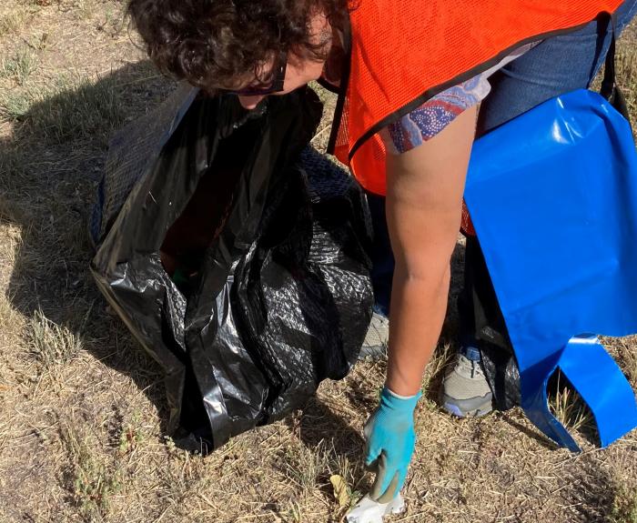 A woman removes litter from near a highway.