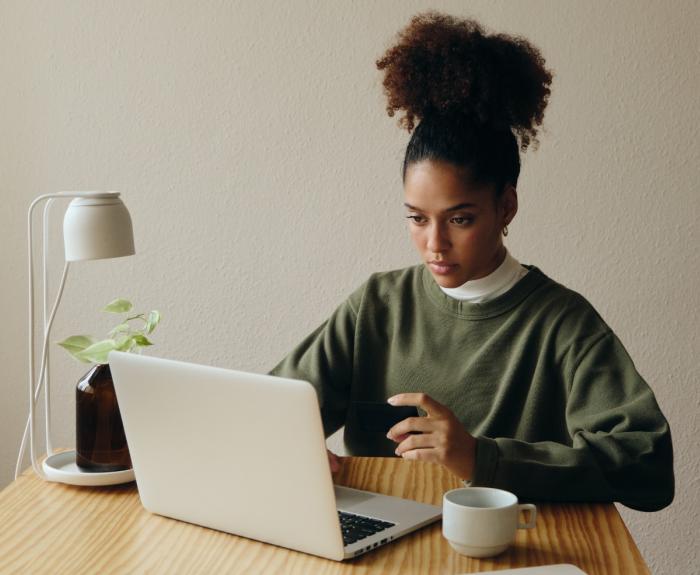 A woman sits at a table, working on a computer.