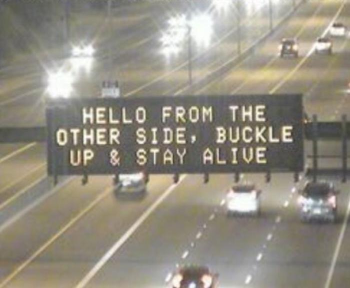 An overhead message board displaying a traffic safety message on a highway.