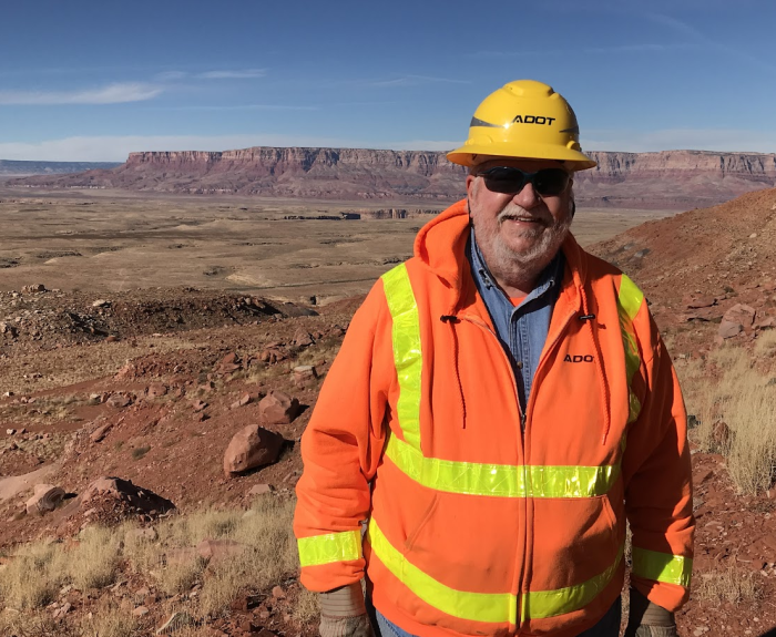 ADOT Geologist Jim Lemmon, decked out in safety gear, poses in front of a desert landscape