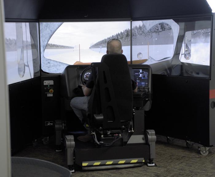 A person sits in the driver seat of a snowplow simulator.