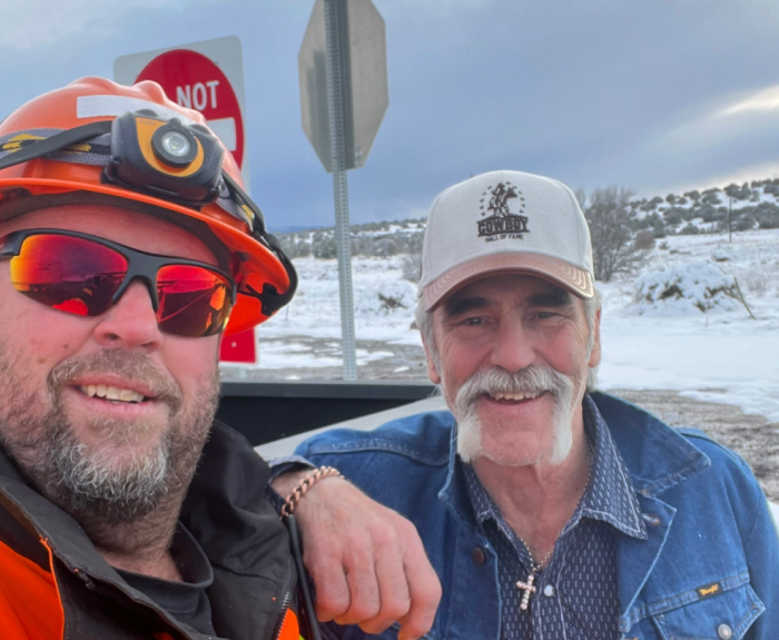 Two men pose near a highway during winter.