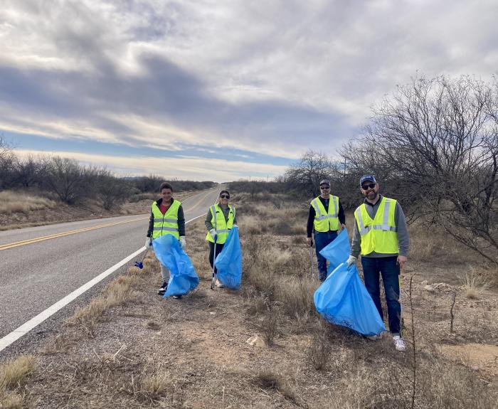 Four volunteers all holding blue trash bags while cleaning up the highway.