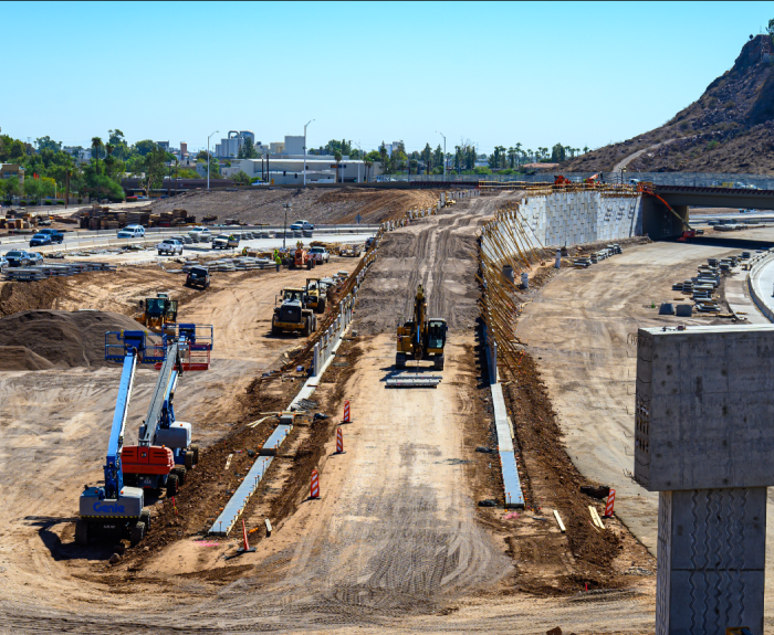 Multiple construction vehicles in the foreground with Interstate 10 in the background. These vehicles are working on the Broadway Curve Improvement Project.