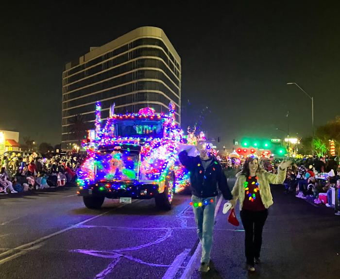 Two ADOT volunteers walking down the street in front of a semi truck decked out in Holiday lights for the Electric Light Parade.