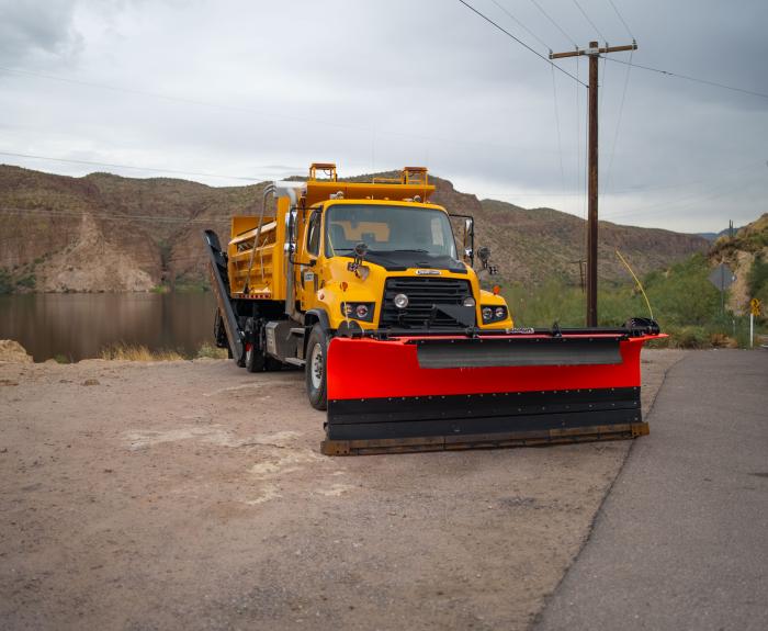 A snowplow in front of a lake and mountains.