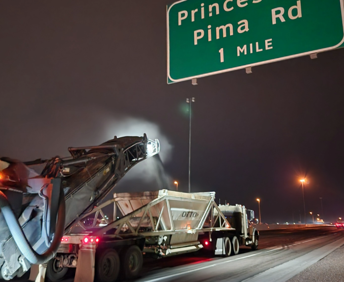 Heavy machinery removes the top layer of asphalt from a freeway at night.
