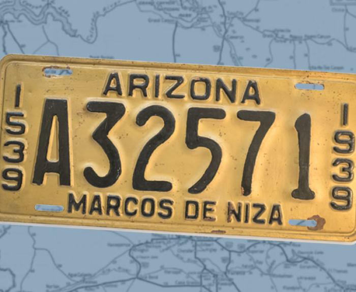 A yellow license plate with black lettering and numbers atop a map of Arizona.