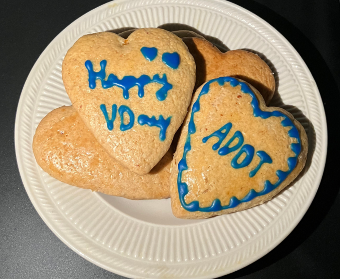 Heart shaped cookies with "Happy V-Day" and "ADOT" written on them in icing.