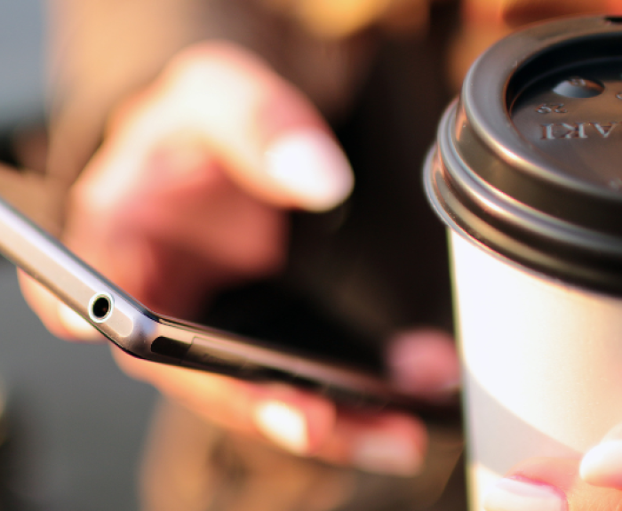 A cell phone is held in a person's hand and a coffee cup is in the other hand.