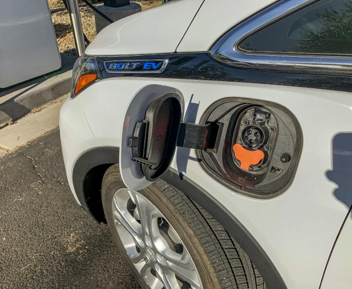 An electric vehicle with an open charge port is parked at a charging station.