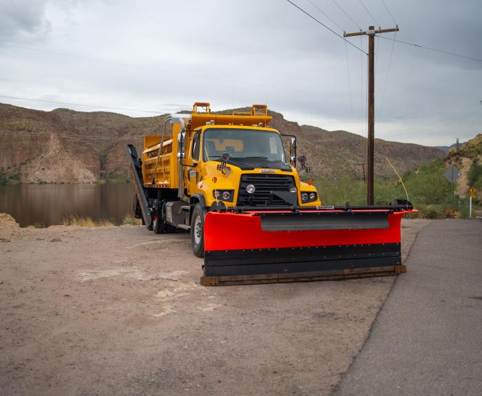 A snowplow parked in front of a lake and mountains.