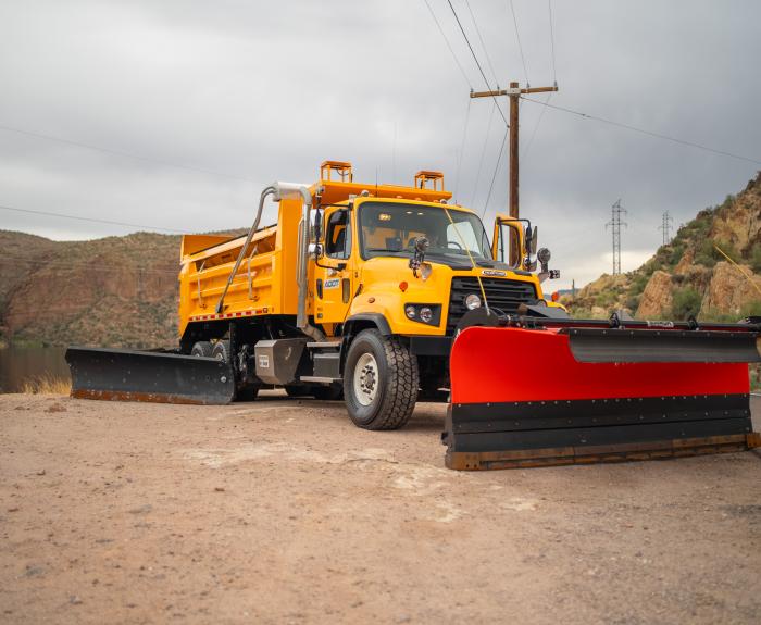 Snowplow parked in front of a lake and mountains