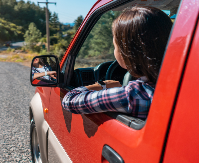 A person in a red car looking out their window to the road in front of them.