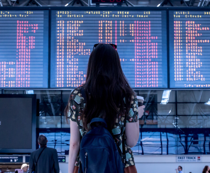 A woman stands in an airport, looking at a board the displays arrival and departure times.