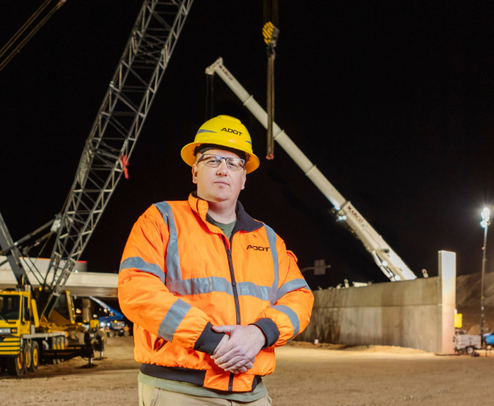 A man in an orange reflective gear stands in a construction area.