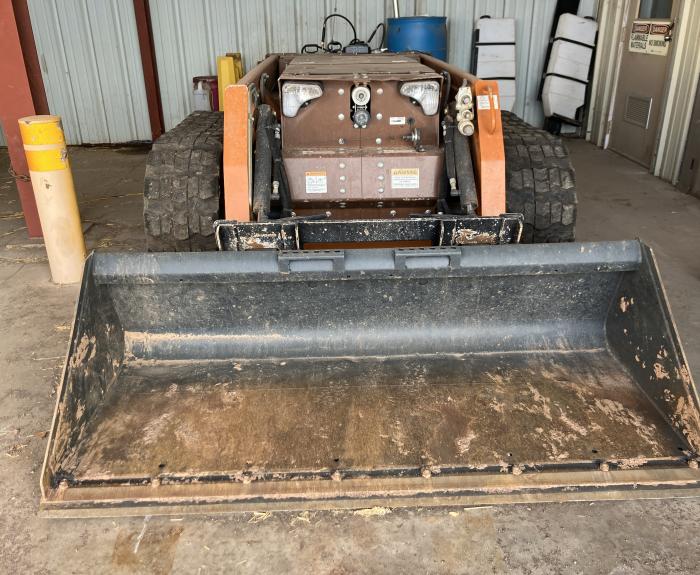 A remotely-controlled skid steer is parked in an equipment garage.