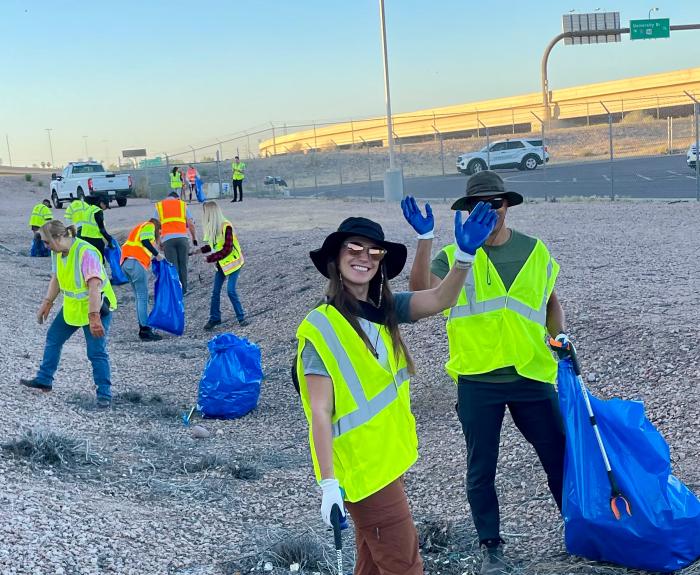 A group of volunteers pick up litter near a highway.