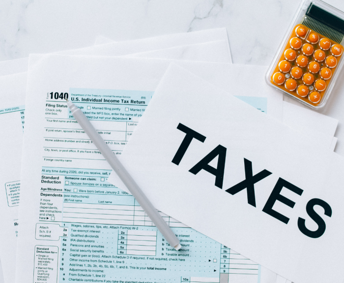 A calculator and a tax form with a pen on top. Also a sign with the word "Taxes" written on it.