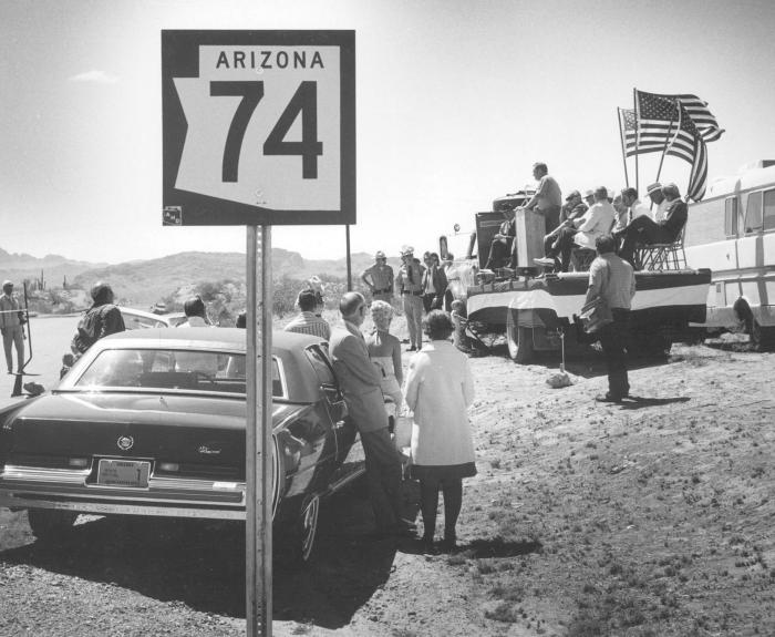 In a black and white photo from 1974, people gather at the opening of a rural highway.