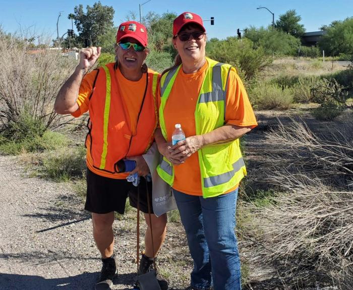 Two people pose for a photo during a litter clean-up event near a road.