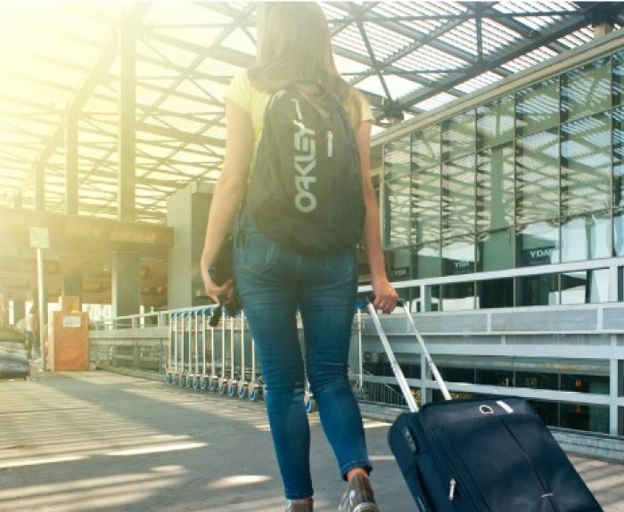 A woman walks with a carry-on bag at an airport.