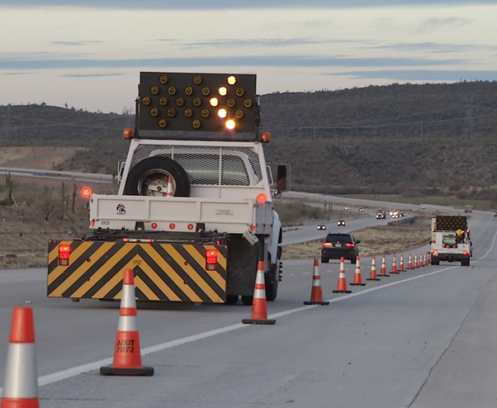 An ADOT cone truck is laying down traffic cones and followed by an attenuator truck in a worzone.