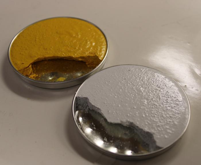 Two small metal tins filled with thick, textured substances: one with yellow paste and one with white paste. Both have a portion scooped out, showing the metal bottom of the tins.