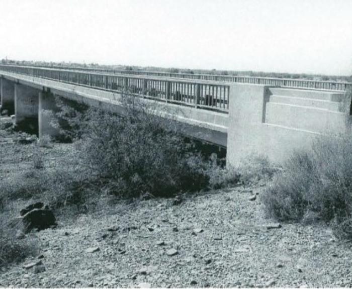 A long, narrow concrete bridge stretches across a dry, rocky landscape with sparse vegetation.