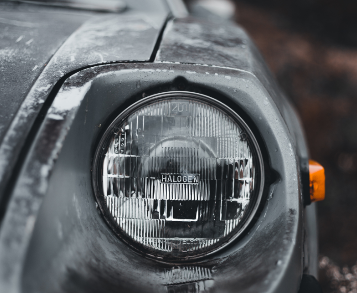 The headlight of a black car showing its age with peeling paint.