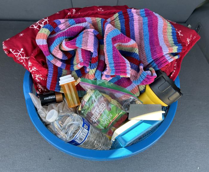 A basket filled with blankets, scarves, water, first aid kit and more