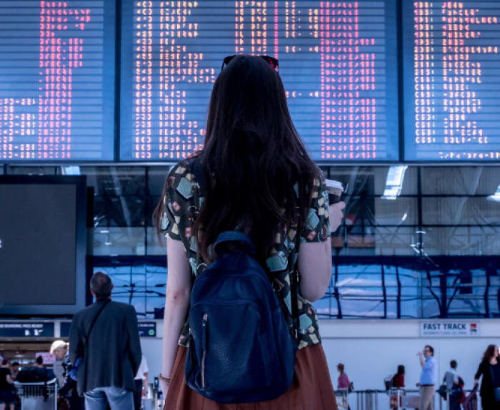 A woman stands in an airport, looking at a board the displays arrival and departure times.