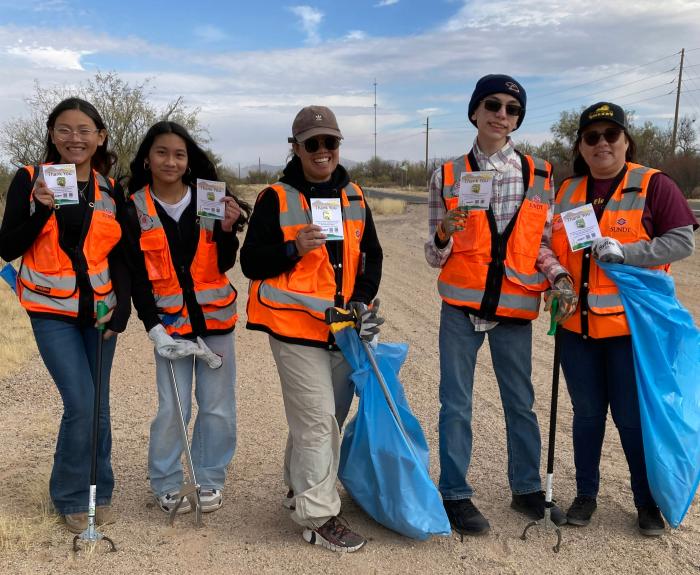 A group of students participate in an Adopt-a-Highway clean-up event along a rural highway.