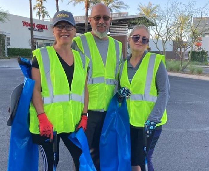Three people in yellow safety vests pose for a picture in a parking lot.