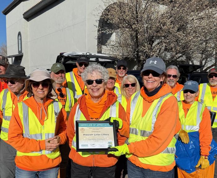 A group of people in orange and yellow safety vests pose for a photo.
