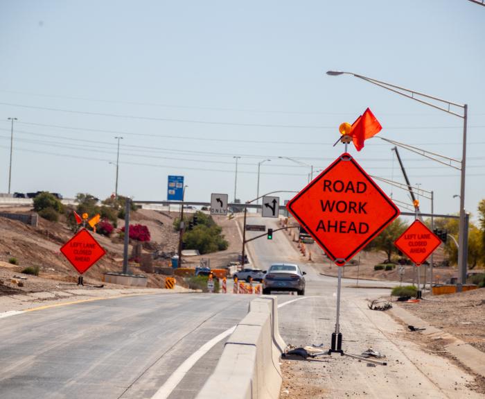 An orange sign in a highway work zone warning of road work ahead.