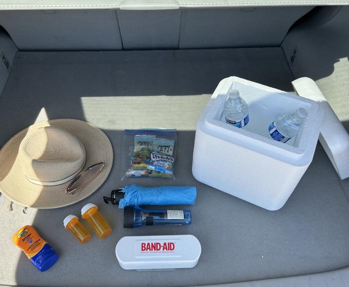 Items that should be in a car travel safety kit, including extra water, first-aid kit, prescription medication, sunscreen and snacks, are in the trunk of a car.